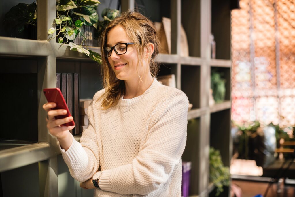 Smart woman checking iPhone by shelf